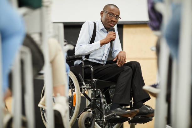A man in a wheel chair holding a microphone talking to a group of people.